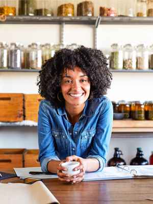 Smiling business owner leaning over her list of available coffees and teas, holding a coffee cup