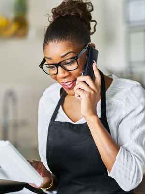 Smiling woman speaking to a customer on her mobile phone while using her sleek PayPal Zettle Virtual Terminal