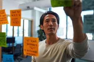 A man looking at some post its glued to a glass in front of him.