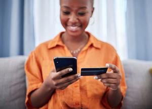 A woman looks at her phone while holding up her balance transfer credit card.