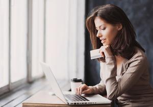 A woman holds her credit card and makes a purchase on her laptop.