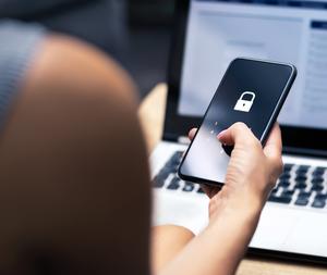 A woman is using a smartphone in front of a laptop.