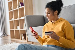 A woman holds up a gift card while looking at her phone.