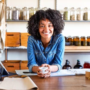 Smiling business owner leaning over her list of available coffees and teas, holding a coffee cup