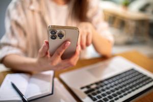 A woman sits in front of her laptop and a notebook, and tracks her savings on her phone.