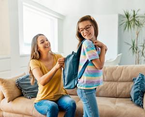 A mom helps her young daughter try on a new school backpack