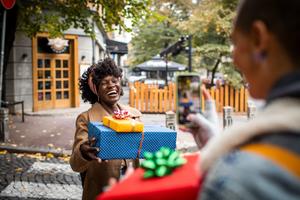 A woman smiles while giving gifts to a friend