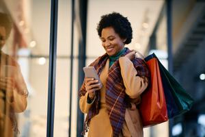 Happy woman texting on cellphone while doing holiday shopping