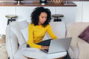 A woman reviews her savings account interest on her laptop and paper statements.