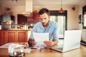 A man reviews his bank statement and monitors financial transactions on his laptop.