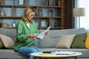 A woman looks worriedly at a document and holds her phone.