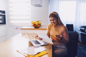 A woman sits in her kitchen and smiles looking at her high yield savings account statement.