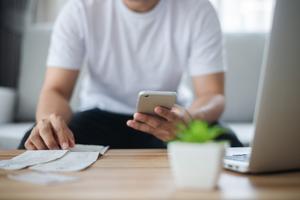 A man practices money management and reads receipts while typing into his phone