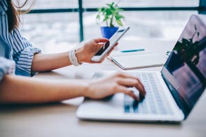 A woman types a one-time password from her phone into her laptop.