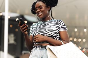 A woman holds a shopping bag and looks at rewards on her phone.