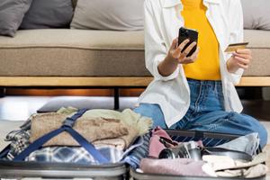 A woman packs a suitcase and types her travel points credit card details into her phone.