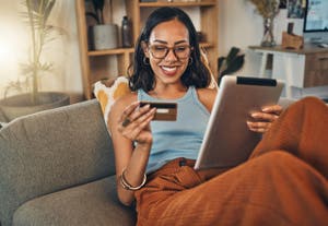 A woman sits on a sofa and looks at her credit card