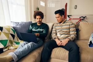 Two men seated on a couch, engaged with a laptop placed on their laps, sharing ideas and collaborating together.